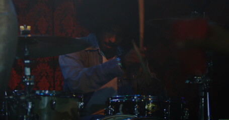 Playing Indian drummer hitting drums and cymbals on club stage, with denim jacket and drumsticks