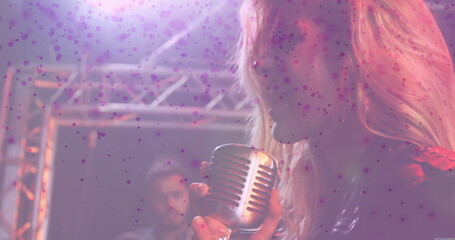 Singing female vocalist holding vintage microphone on dim stage, with electric guitar and truss