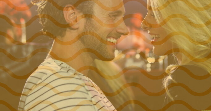 Smiling couple leaning close in lounge bar, wearing striped shirt under glowing pendant lamps