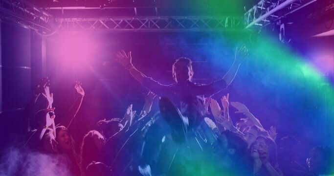 Crowd-surfing male fan riding over cheering crowd inside club, with stage lights and metal truss - Powered by Adobe