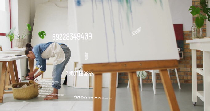 Bending over wicker basket woman wearing denim shirt, apron in art studio, with easel copy space