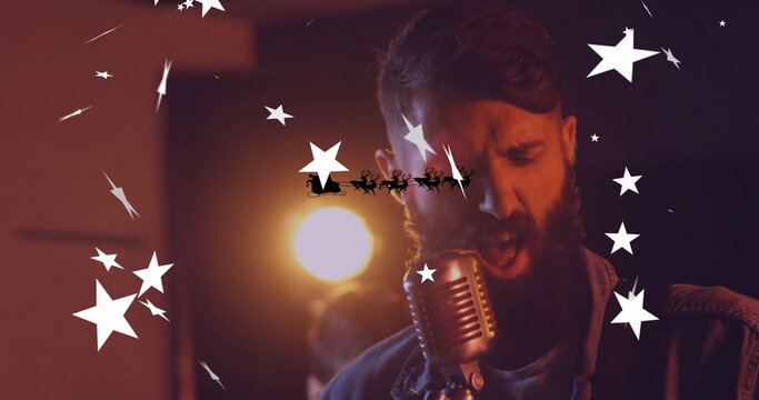 Leaning denim-clad singer into mic on stage in spotlight with Santa sleigh silhouette and overlays