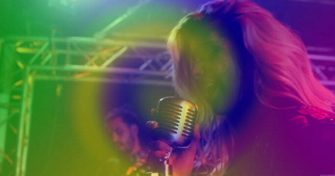 Performing singer wearing leather jacket gripping microphone on stage with guitar, lights and haze