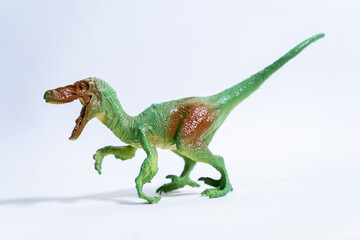 Green and brown velociraptor toy dinosaur running on white background