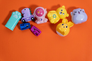 Colorful pencil sharpeners shaped like cute animals and objects resting on orange surface