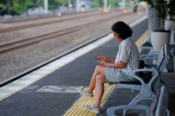 A woman is sitting alone at a train station, looking at her phone © Bunda