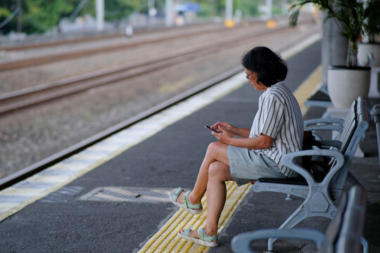 A woman is sitting alone at a train station, looking at her phone