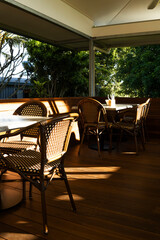 Glass House Mountains, Australia - 26 June 2025 : Glasshouse Plantation, a sunlit outdoor deck with wicker chairs and tables.