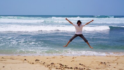 A young man jumps for joy and freedom on a beautiful beach in the tropics on a sunny day.