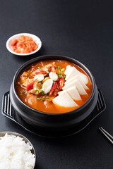 Korean food (Kimchi Jjigae), Kimchi soup with tofu, pork, scallion and chili in Korean stone bowl eating with cooked rice and kimchi on black background