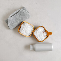 Natural spa, wellness, bath accessories as minimal flat lay pattern, sea salt flakes in wooden bowls, soft gray towels, brush, reusable cotton pads, grey conctrete background, top view neutral colors