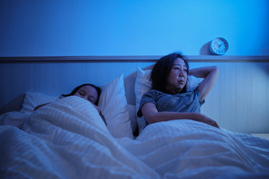 Asian single mum is sleepless, stressed, and worried awake at night after divorce near her daughter, insomnia illness in bedroom, mature and menopausal woman, family healthcare problem, lifestyle.