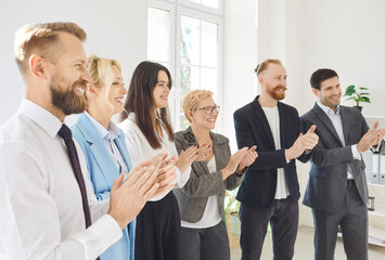 Group of young business people applauding standing in a row in office. Friendly smiling successful coworkers and company employees clapping a colleague on a meeting or business conference.