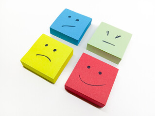 four colored sticky notes with hand-drawn faces representing various emotions, arranged on a white background.