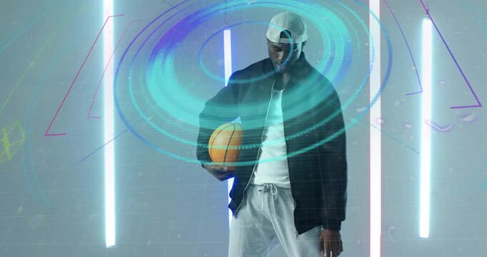 Male athlete holding basketball starting neon rings swirling in studio, dribbling for sports tech - Powered by Adobe