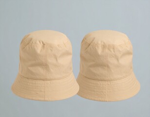 Two beige fabric bucket hats displayed against a light blue background, showcasing a simple and casual headwear accessory.