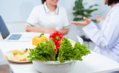Naklejka premium Professional Asian female nutritionist giving nutritional counseling to female patient sitting at clinic table discussing diet, health goals, meal plans and strategies for long-term wellness
