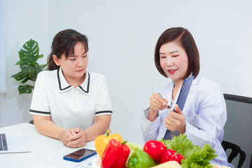 Professional Asian female nutritionist giving nutritional counseling to female patient sitting at clinic table discussing diet, health goals, meal plans and strategies for long-term wellness