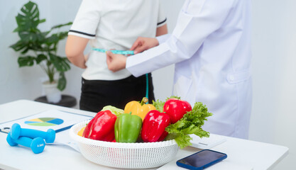 A middle-aged Asian female dietitian conducts a health consultation with a middle-aged Asian female patient at a table, focusing on weight loss, waist measurement, BMI, diet control,overall wellness