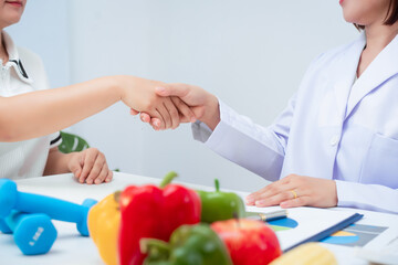 Professional Asian female nutritionist giving nutritional counseling to female patient sitting at clinic table discussing diet, health goals, meal plans and strategies for long-term wellness