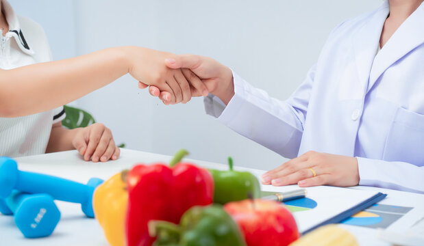 Professional Asian female nutritionist giving nutritional counseling to female patient sitting at clinic table discussing diet, health goals, meal plans and strategies for long-term wellness