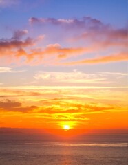 A breathtaking sunset casts vibrant hues of orange, pink, and purple across the sky, reflecting on the tranquil ocean waves below, creating a serene atmosphere.