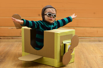 Flying child flying with cardboard wings. Kid dreams of pilot. Child fly with paper plane. Child in aviator helmet indoors. Child flying with toy airplane. Dreaming baby flying in cardboard box.