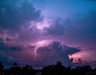 Dramatic purple lightning strikes through a stormy sky above a dark silhouetted landscape