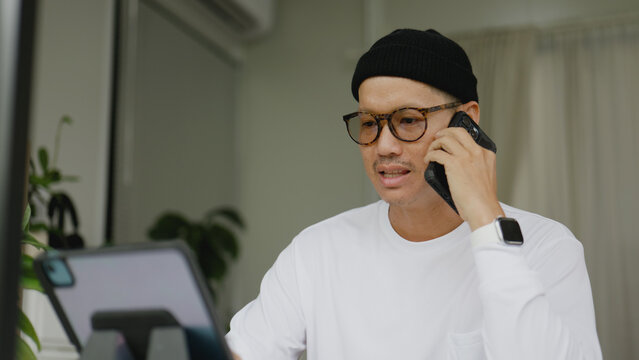 Asian man multitasking with his smartphone while checking information on a tablet. - Powered by Adobe