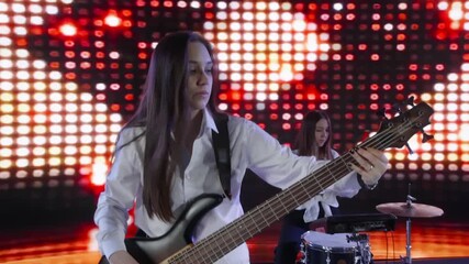 Young female musician energetically playing bass guitar on stage with illuminated led wall in the background, creating a vibrant and captivating performance - Powered by Adobe