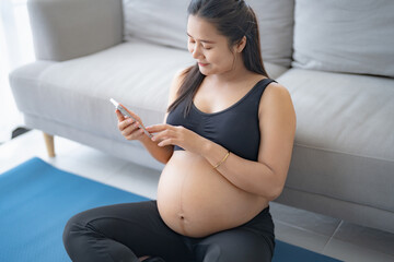 Pregnant asian woman practicing yoga at home and using phone relaxation and Self-care during Pregnancy mother mindfulness Positive life moment in pregnancy time