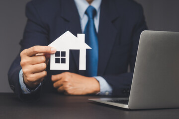 Businessman presenting housing investment concept with house model near laptop.