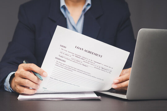 Businessman reviewing loan agreement document at office desk with laptop in view.