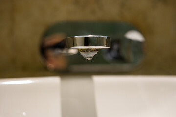 Close-up view of a metallic water faucet with a droplet about to fall, symbolizing daily life details, household utility, and the importance of water conservation.