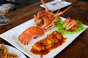 Top view of lobster with sauce and fresh garnish on a dining table, taken in a restaurant environment. Balanced natural lighting emphasizes vibrant food colors and appetizing details.