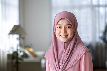 Portrait of asian muslim woman with hijab headscarf sitting on the sofa couch at home while looking...