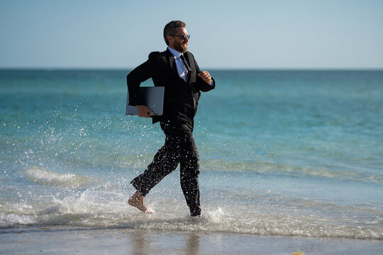 Summer business. Freelancer run on summer sea beach. Businessman in wet suit jump in sea water. Crazy business summer vacation. Funny businessman with laptop in suit on beach. Hot summer. - Powered by Adobe