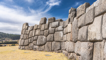 The wall of the ancient Inca fortress Sacsayhuaman. Amazing unique stonework. Ashlar polygonal masonry. Boulders are closely adjacent to each other. The grass in the clearing. Blue sky, clouds. Peru.