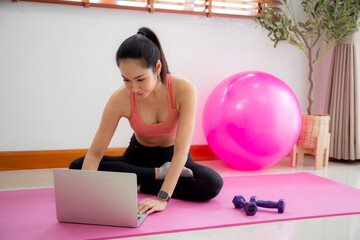 Young asian woman watch laptop for practice yoga and workout in living room at home, woman using chat bot on notebook with artificial intelligence with for training and exercise, sport and wellbeing.
