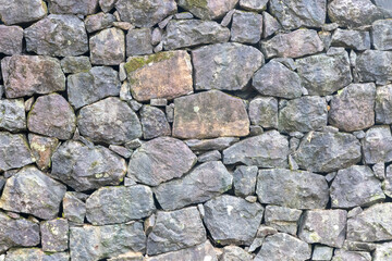 A weathered, dry-laid stone wall with moss and lichen. The stones vary in size and shape, creating a rustic, natural texture