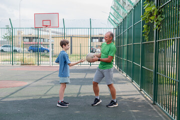 Father teaches his son how to play basketball. The boy throws the ball into the hoop at the playground. Generation. Sports. Hobbies