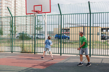 Father teaches his son how to play basketball. The boy throws the ball into the hoop at the playground. Generation. Sports. Hobbies