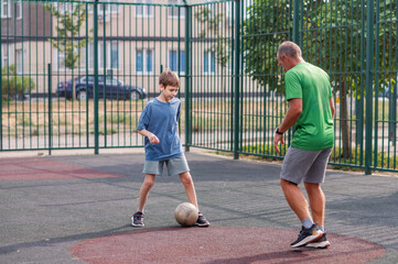 A man and a boy are running around the playground, kicking a ball, and playing soccer. The father is teaching his son how to play soccer. Family values. Sports