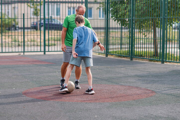 Fototapeta premium A man and a boy are running around the playground, kicking a ball, and playing soccer. The father is teaching his son how to play soccer. Family values. Sports