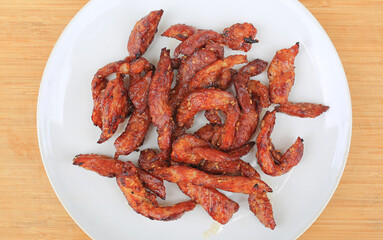 Deep fried sun-dried pork on white plate against wooden background, Thai style food. Top view.