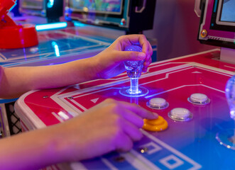 A person's hands gripping a joystick and pressing buttons on an arcade game machine. Nostalgia, fun, and entertainment from classic arcade gaming concept.