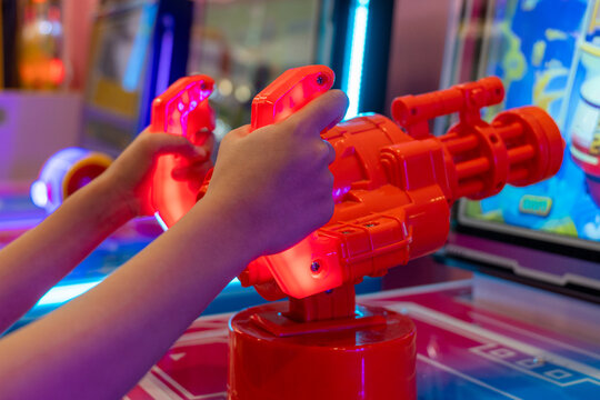 A close-up of a hands holding a red, futuristic-looking toy gun from an arcade game. The thrill and action of playing a video game in an arcade setting. - Powered by Adobe