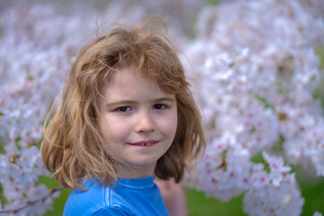 Cute blonde kid boy in spring garden. Little child under a blossom tree. Happy kid playing under blooming cherry tree. Kid with flower on Easter. Adorable kid in blooming cherry garden on spring day.