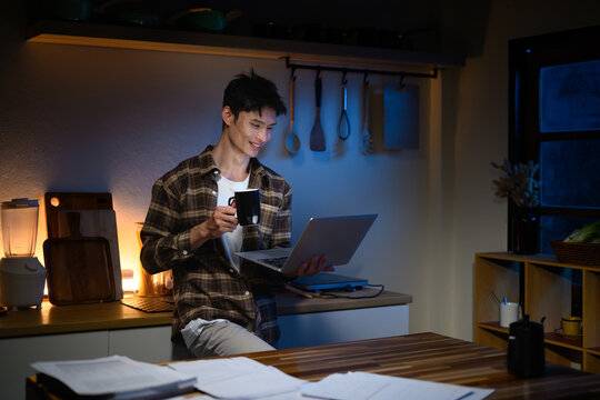 Relaxed man enjoying coffee while working on laptop late at night at home