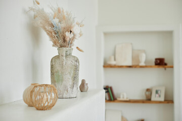 Still life showing rustic ceramic vase with dried grass arrangement standing on ledge, small woven...